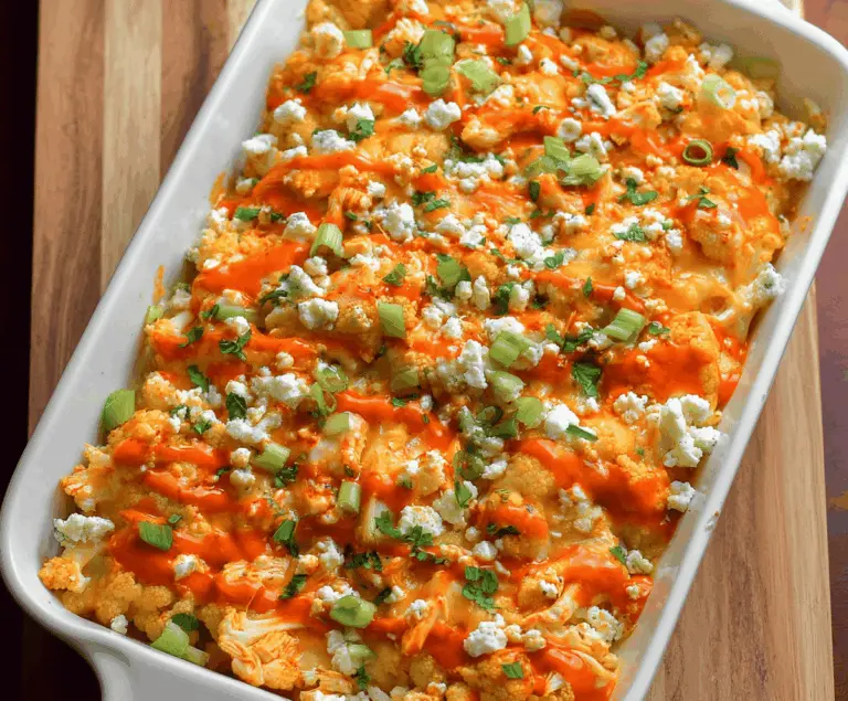 Creamy Buffalo Chicken Cauliflower Casserole topped with melted cheese and garnished with fresh green herbs, perfect for a spicy, low-carb dinner option.