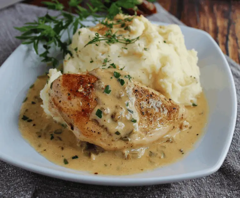 Juicy chicken breast topped with creamy Dijon sauce served alongside smooth mashed potatoes on a white plate.