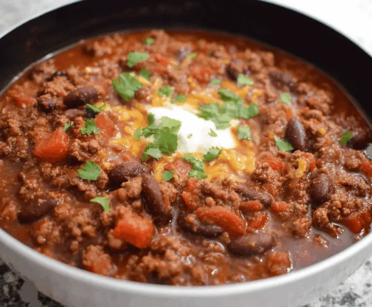 Hearty ground beef stovetop chili served in a bowl with beans, tomatoes, and spices, topped with shredded cheese and fresh cilantro