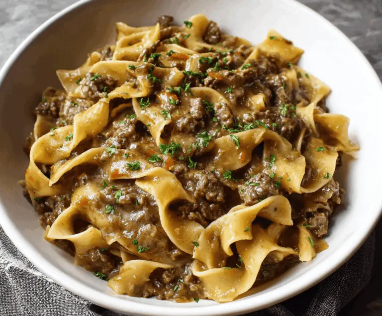 Homemade stovetop beef and noodles served in a white bowl with tender beef chunks and hearty noodles, garnished with fresh herbs.