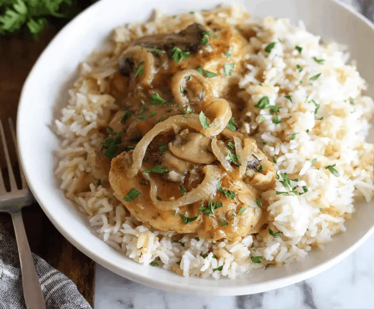 Creamy smothered chicken served over flavorful rice, topped with herbs and gravy, perfect for a hearty and comforting meal.