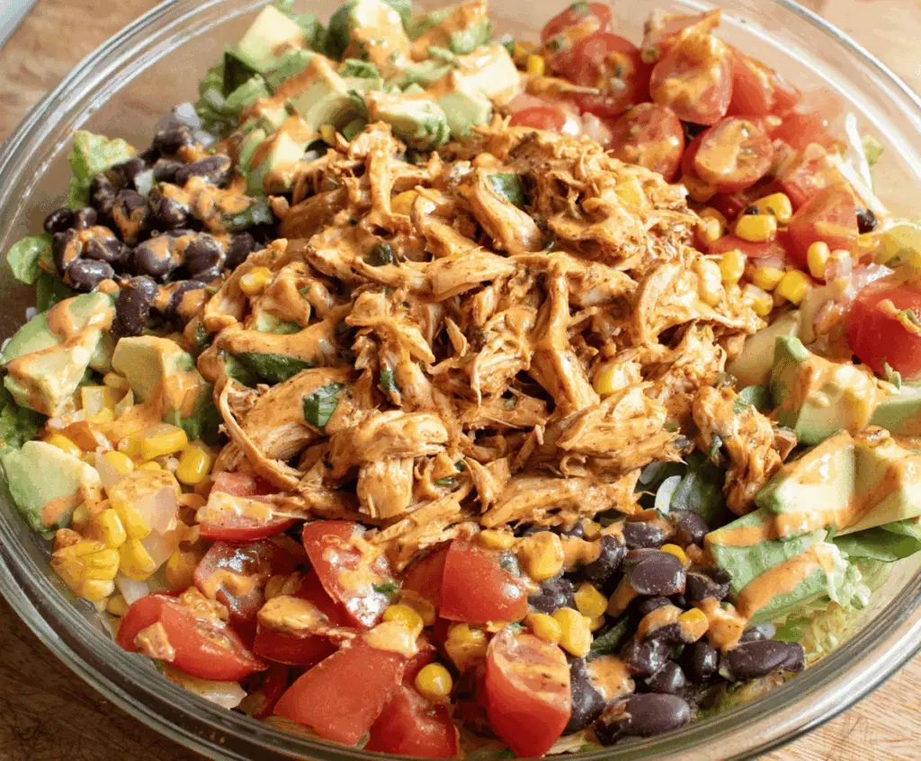 Fresh Southwest Chicken Salad featuring grilled chicken, mixed greens, corn, black beans, cherry tomatoes, shredded cheese, and a spicy southwest dressing in a bowl