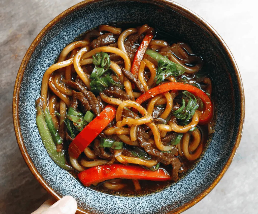 Delicious beef black pepper udon noodles dish garnished with green onions and sesame seeds on a white plate