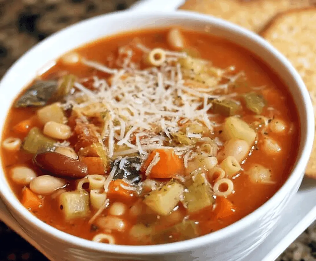 A steaming bowl of Classic Minestrone Soup filled with vegetables, pasta, and beans, garnished with fresh herbs in a rustic bowl.