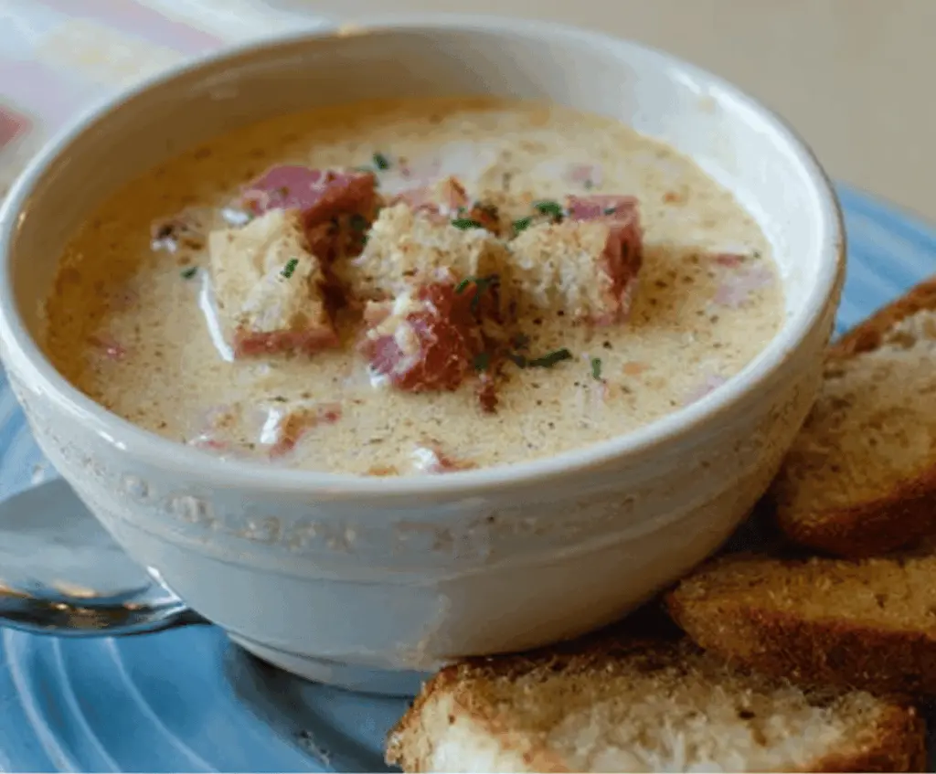 A bowl of creamy Reuben soup topped with melted cheese, sauerkraut, and rye croutons, served with fresh parsley on a rustic wooden table.