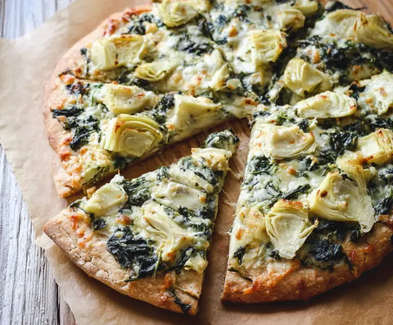 Delicious high protein spinach and artichoke pizza topped with melted cheese and fresh greens.