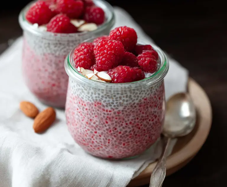 Creamy vegan raspberry chia pudding topped with fresh raspberries in a clear glass bowl.
